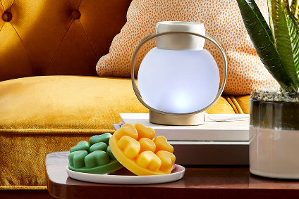Yellow sofa with a small table holding a plate of melts and a decorative ScentGlow Warmer, with a plant in the background.